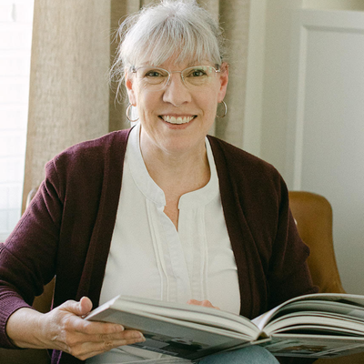 Kendra Burrows woman sitting holding book open glasses, gray hair and dark sweater